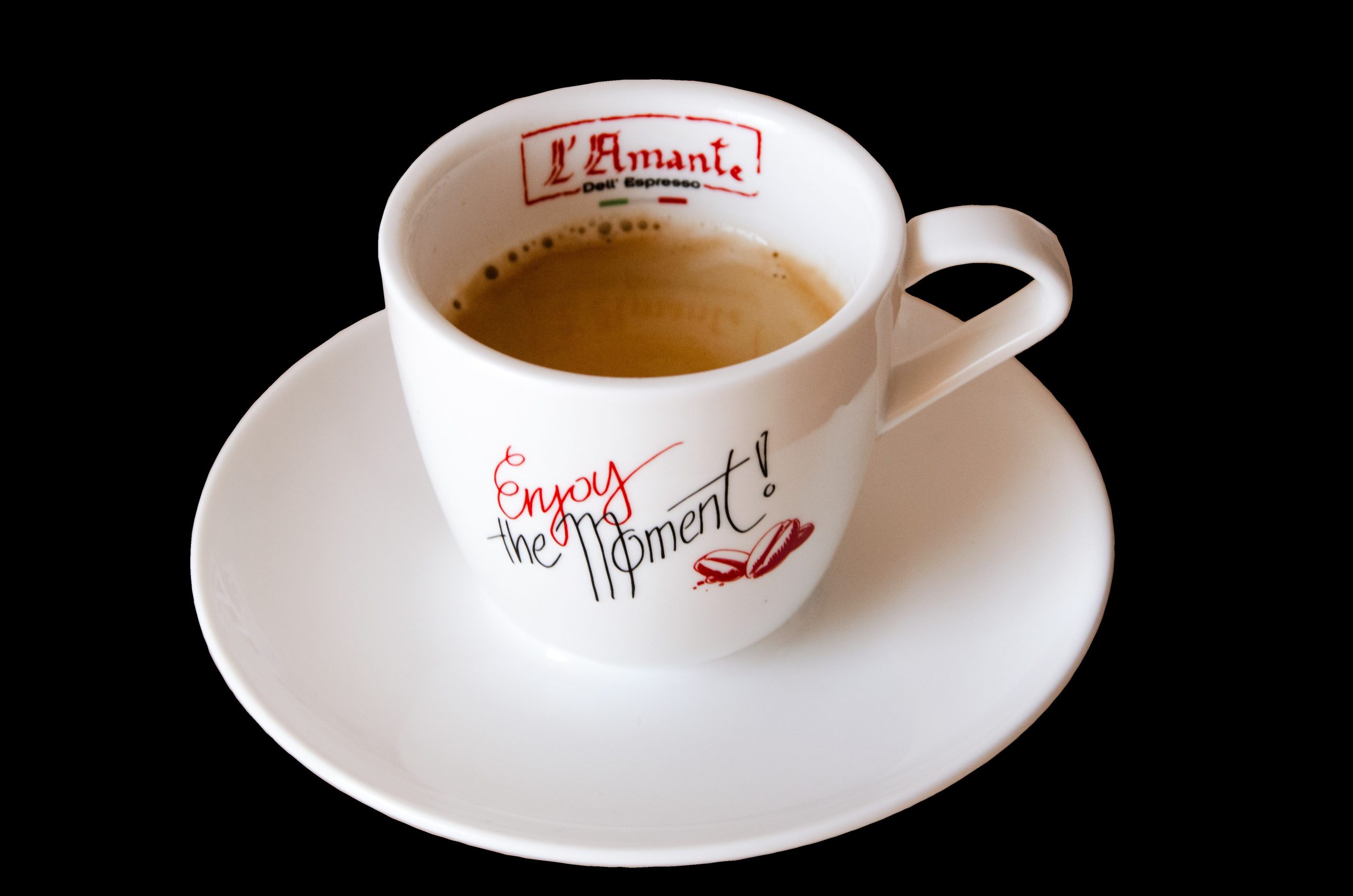 L´Amante_Kaffeetasse - White ceramic coffee cup on a saucer, viewed from above, with red script reading 'Enjoy the moment' against a black background.